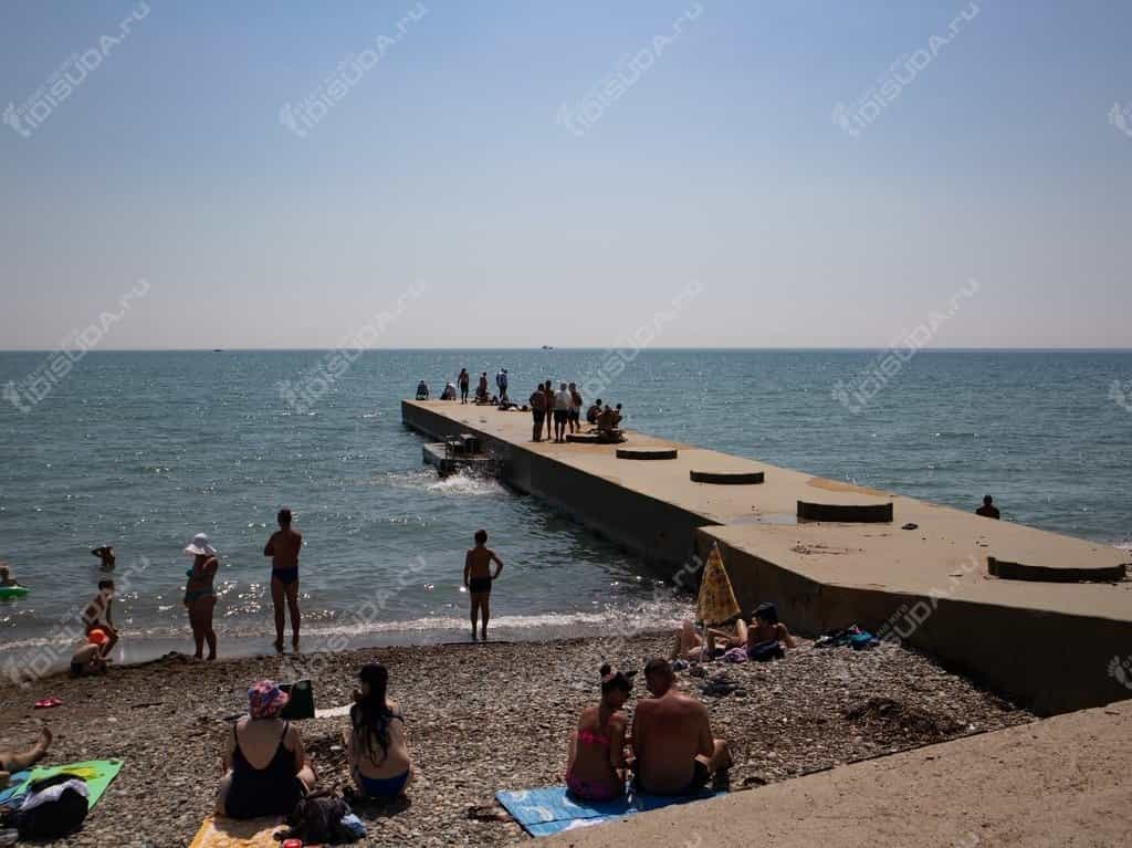 Галечный пляж с волнорезом в Дивноморском, туристы загорают и купаются