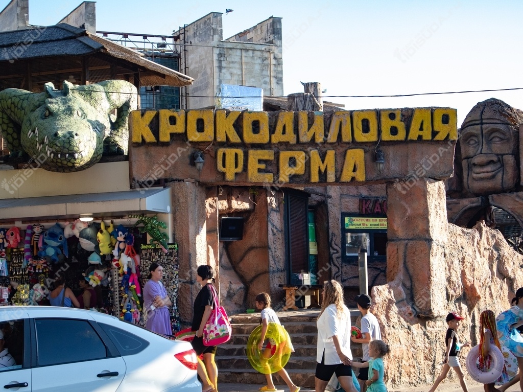 вид с улицы на террариум Крокодиловая ферма, скульптура крокодилов, туристы в Анапе, лотки с товарами, автомобиль
